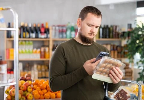 Male purchaser scanning QR code or barcode of canned champignons mushrooms in Stock Photos