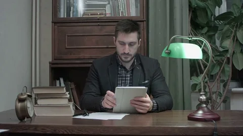 Male researcher using digital tablet and making notes sitting at his study desk Vídeos de archivo 73687232