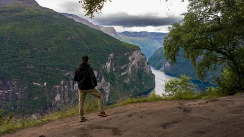 Male runner in black jacket pauses at clifftop vista overlooking deep river v Fotos Stock