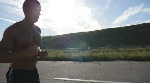 Male runner jogging during workout training on country road at sunset. Slowmo Stock Footage
