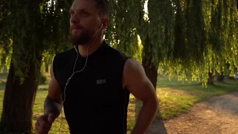 Male runner running down the road in the park at sunset Stock Footage 79034382