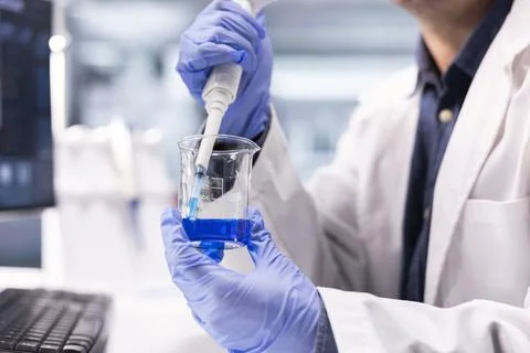 Male scientist performs compound transfer with pipette into jar for experiment Stockfoto's