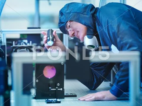Male Scientist In Protective Clothing Uses Torch To Inspect Laser Crystal In