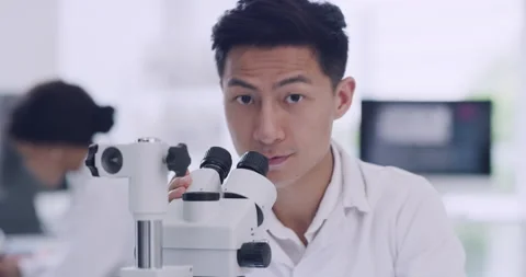 A male scientist in a research lab using a microscope. Portrait of a happy young Stock Footage 200490320