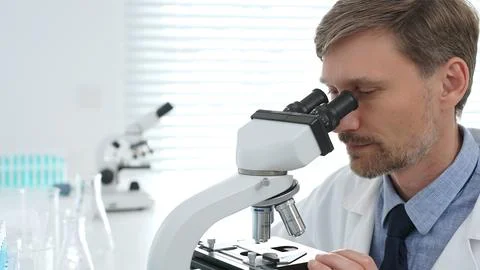 Male scientist using a microscope is doing scientific research in a modern Stock Photos
