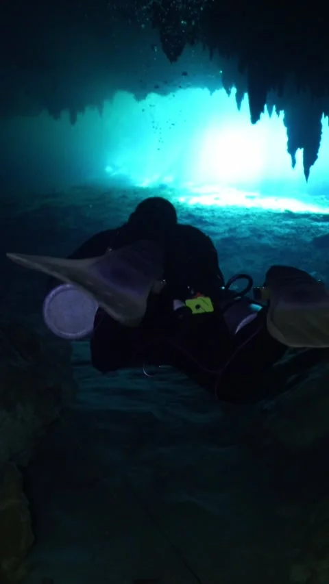 Male scuba diver with a flashlight exploring a dark underwater cave with Vidéo 331340961