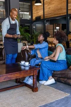 Male server taking order from two women on leather sofa at cafe with tablet, Stock Photos