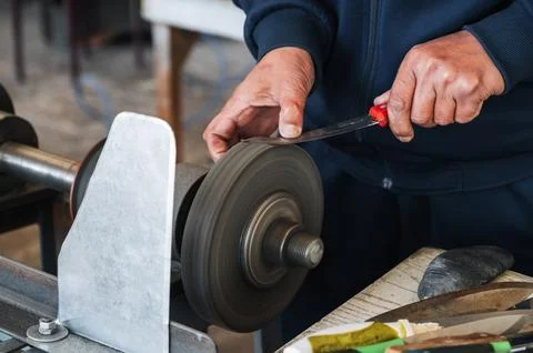 Male sharpener sharpens a knife blade on a knife sharpening machine in workshop Stock Photos