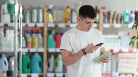 Male shopper checks a QR code on a dishwashing sponge label in a supermarket Stock Footage 314245115