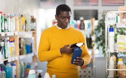Male shopper checks QR code on spray glass cleaner for windows label in Stock-Fotos