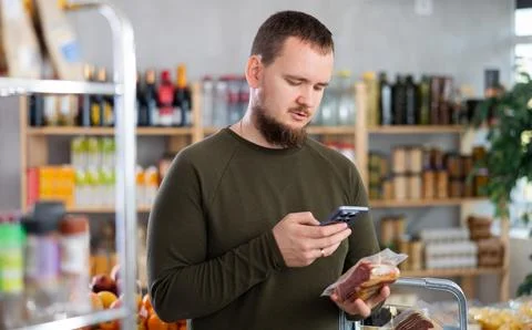 Male shopper scanning QR code on ham label in grocery department of supermarket Foto stock