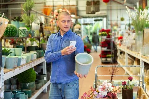 Male shopper scanning qr code on flower pot using smartphone Photos
