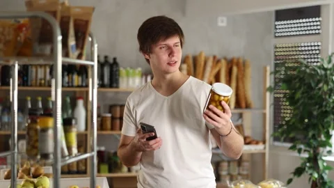 Male shopper scans a QR code on a label of canned olives in a supermarket Stock Footage 306453129