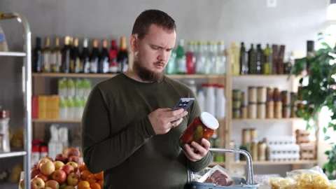 Male shopper scans a QR code on a label of canned cucumbers and tomatos in a Stock Footage 306981691