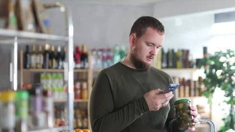 Male shopper scans a QR code on a label of canned cucumbers in a supermarket Stock Footage 306983501