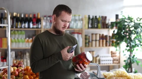 Male shopper scans a QR code on a label of canned tomatos in a supermarket Stock Footage 307065396
