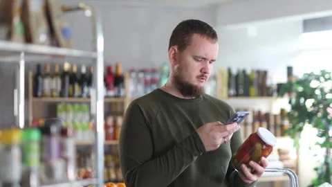 Male shopper scans a QR code on a label of canned cucumbers and tomatos in a Stock Footage 330043095