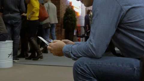 A male sits in a queue, uses smartphone and solves his affairs Stock Footage 102312698