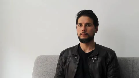 Male sitting on a couch seeing to the front in a concentrating attitude Stock Footage 340583398