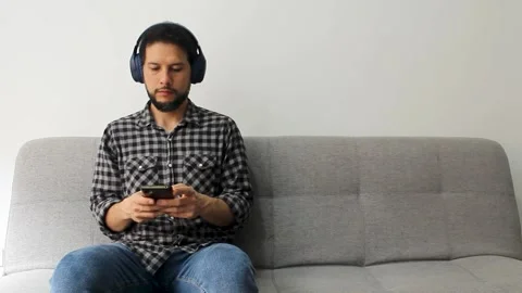 A male sitting at the left side of a couch typing on a smartphone Vídeo Stock 340583504