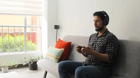 Male sitting at the right side of a couch listening and watching a video Vídeo Stock 340583443