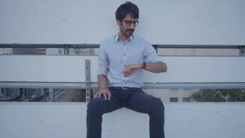 Male sitting on rooftop checking time waiting thinking missing someone shot 3 Stock Footage 293588232