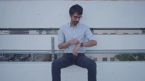 Male sitting on rooftop checking time waiting thinking missing someone shot 2 Stock Footage 293588280