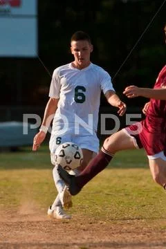 Male Soccer Player Kicks Ball Against Defender Stock Photos