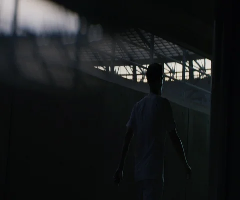 Male soccer player in white jersey walking alone in dark corridor Stock Footage