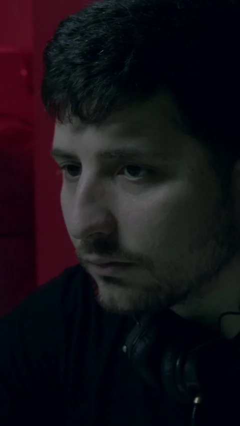 Male software developer with headphones, focused on coding in a dimly lit Stock Footage 313926625