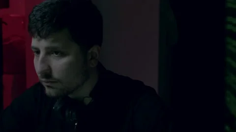 Male software developer with headphones, focused on coding in a dimly lit Stock Footage 314270632