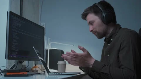 A male software developer makes a videocall with coworkers while sitting at his Stock Footage 199116406