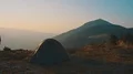 The male stands near the camping tent on the mountain on a sunset background 4k or 4k+ Resolution