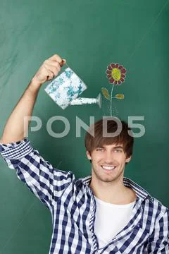 Male student holding watering can with flower drawn on chalkboar Stock Photos