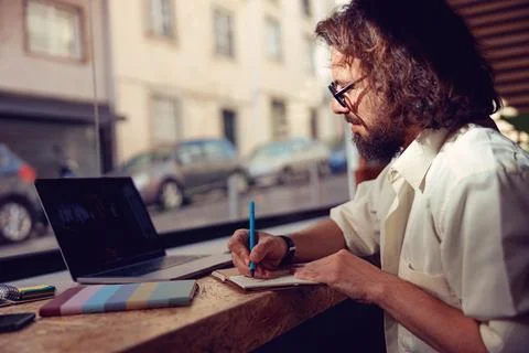 Male student making notes during online lecture while sitting in cafe near Stock Photos