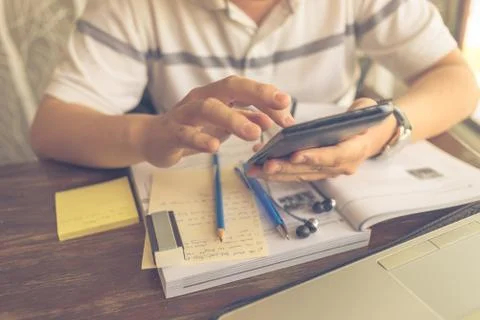 Male student using cellphone while studying with workbook on table Stock Photos