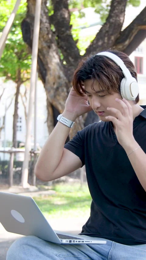 Male Student Using Laptop and Headphones Outdoors on University Campus Stock Footage 334640992