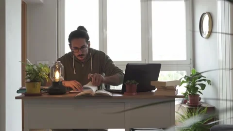 Male studying and taking notes with laptop and books in room with plants Stock Footage 162107051