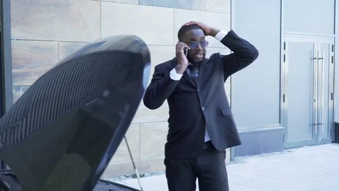 Male in suit arguing over cellphone standing by broken car with open hood, hurry Stock Footage