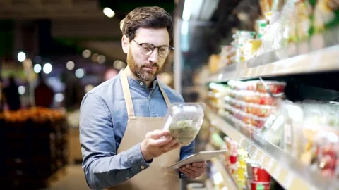Male supermarket worker using digital tablet checking shelves with products  Stock Footage 343615988