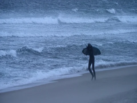 Male surfer walking with surfboard on beach during high tide in slow motion Stock Footage