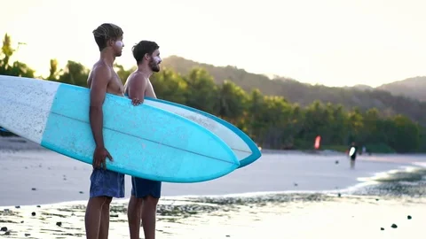 Male surfers standing on beach. Surfer friends holding surfboard  Stock Footage 108564661