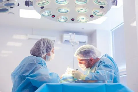 Male surgeon performs surgical procedures in the operating room, while his Stock Photos