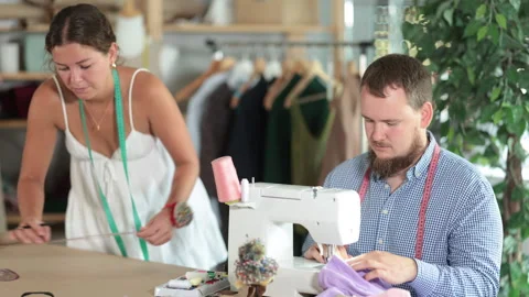 Male tailor sewing garment while female colleague drafting pattern Stock Footage 328141449