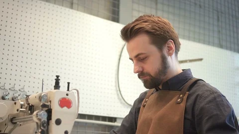 Male tailor using sewing machine to create brown artificial leather bag in Stock Footage 94535042