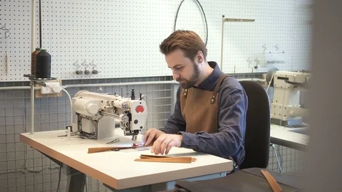 Male tailor working with sewing machine stitching material pieces parts together Stock Footage 121389822