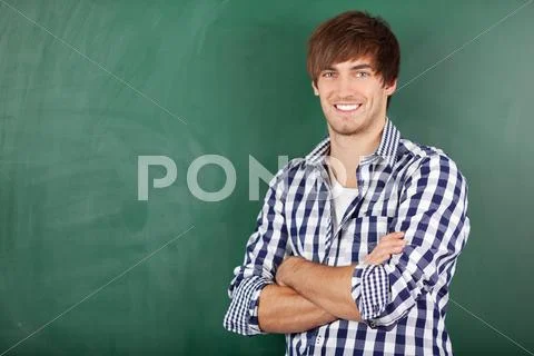 Male teacher with arms crossed standing against chalkboard Stock Photos