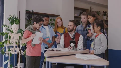 Male teacher explaining topic in textbook to children, look at camera and smile Vídeo Stock 162733208