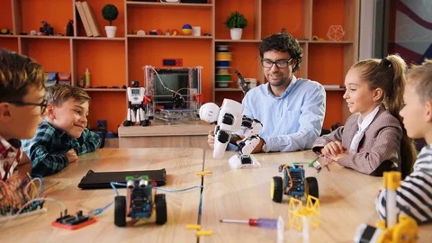 Male teacher with the tablet computer exploring a robot with his pupils in the Stock Footage 82477124