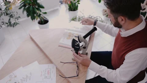 Male teacher using microscope and looking at biology textbook in modern school Video stock 162736461